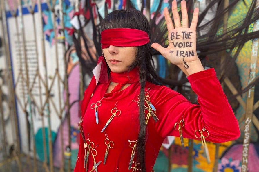 Photo of blindfolded woman with "Be the voice of Iran" written on palm and wearing red clothing adorned with scissors