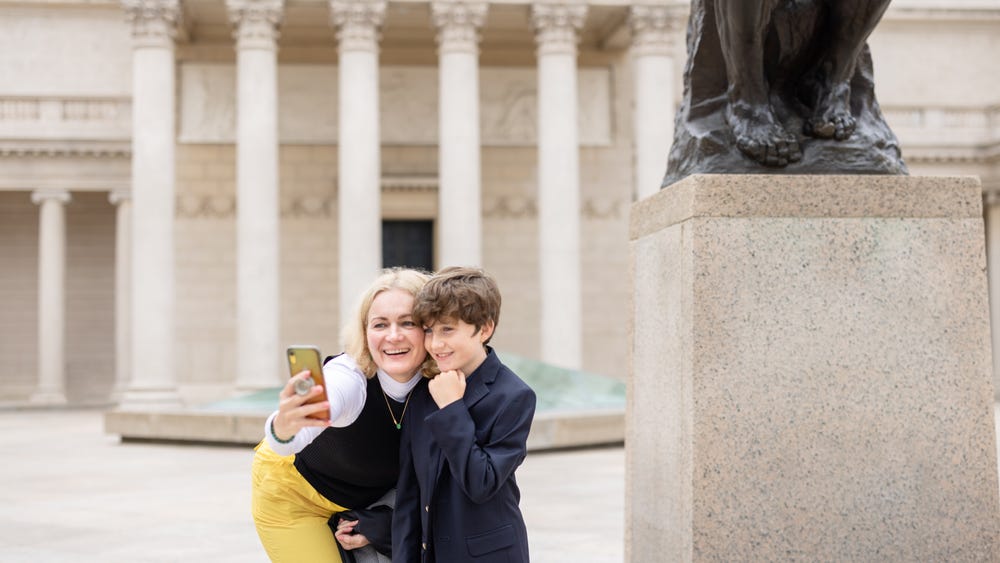 a mom and son take a selfie in front of a statue