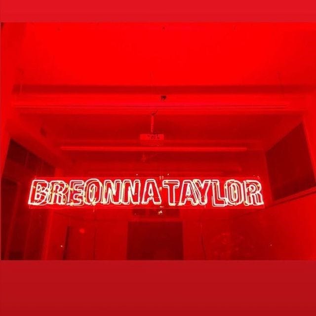red lit room with "Breonna Taylor" in a neon sign.