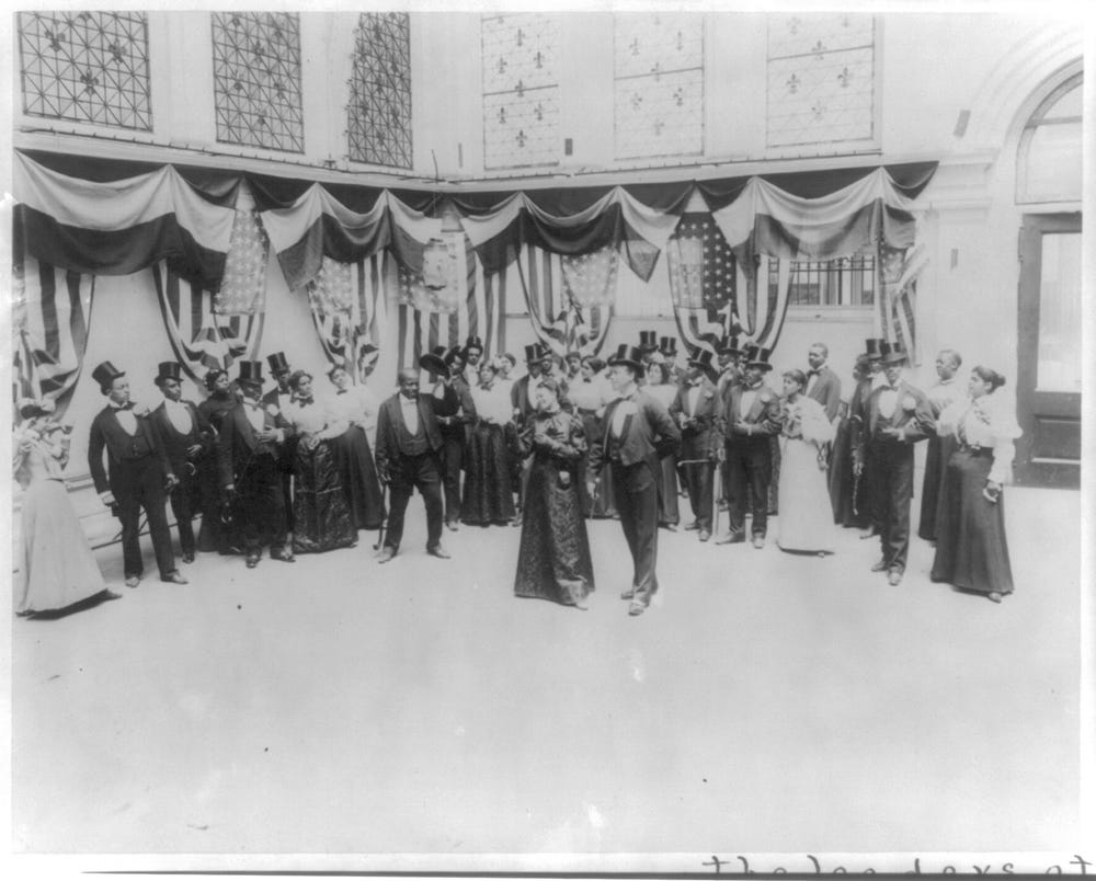 African Americans in formal dress in ballroom doing the cakewalk
