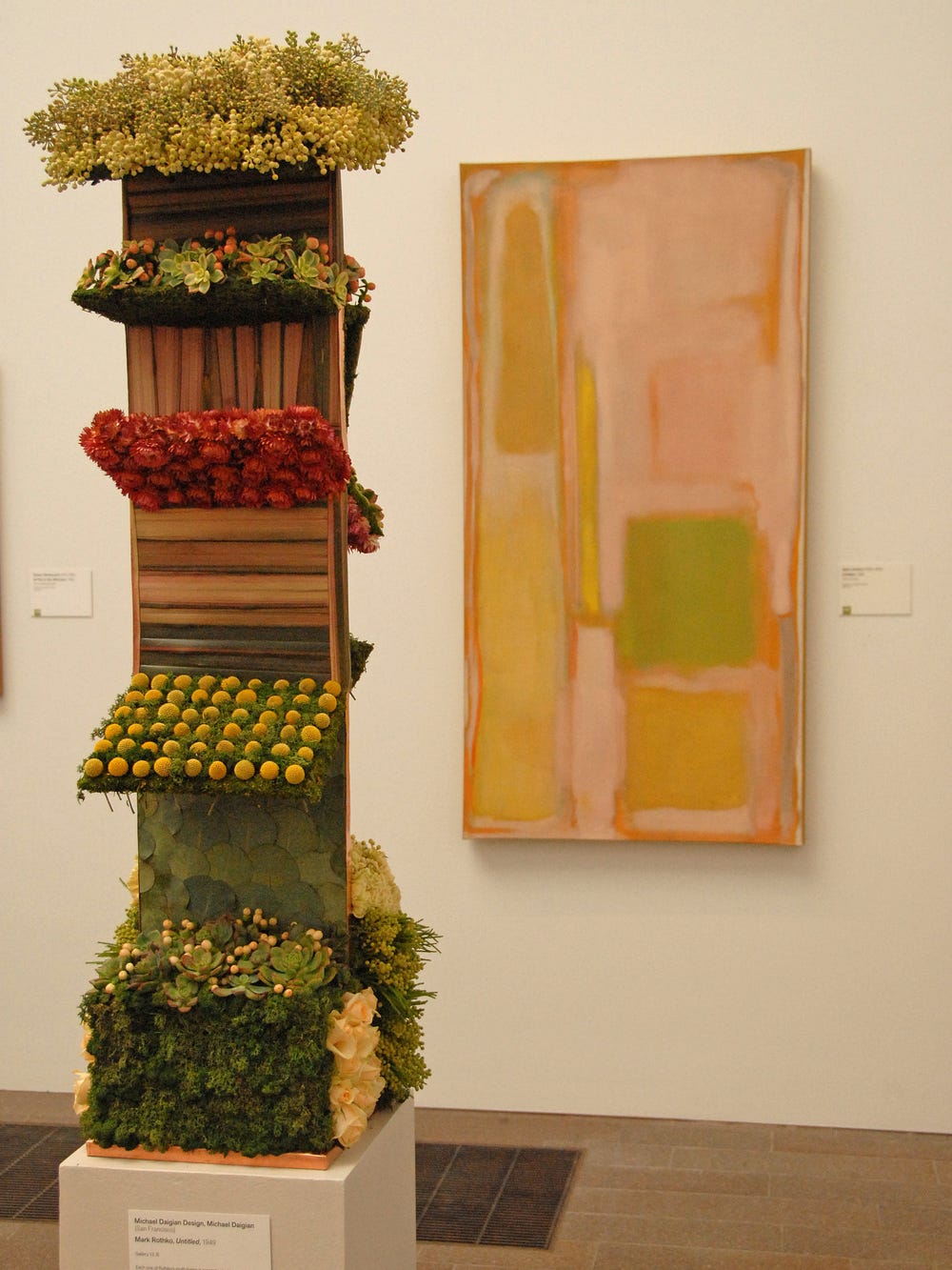 Photograph of green, brown and red floral arrangement in style of painting in background.
