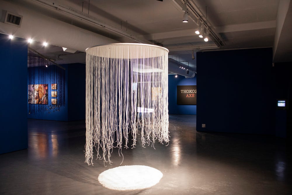 Circular, beaded artwork by Lhola Amira hanging almost to the ground, hovering over a circular bed of salt