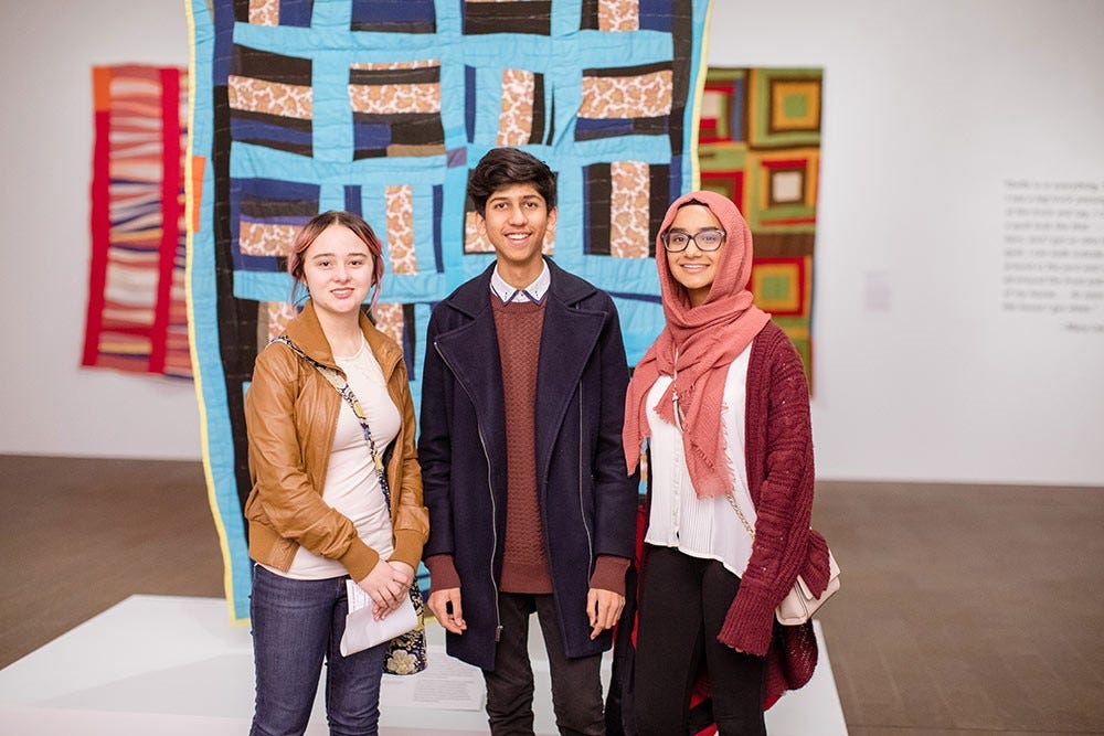 three teens in a gallery in front of a quilt