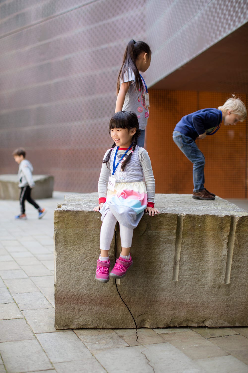 girl sitting on a rock with two other kids standing on it and one in the background