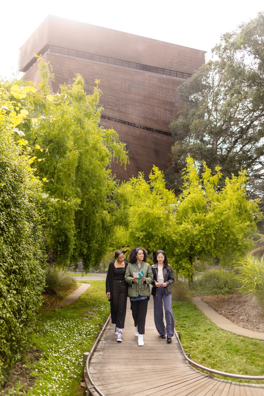 three young women walking in a garden in front of the de Young tower