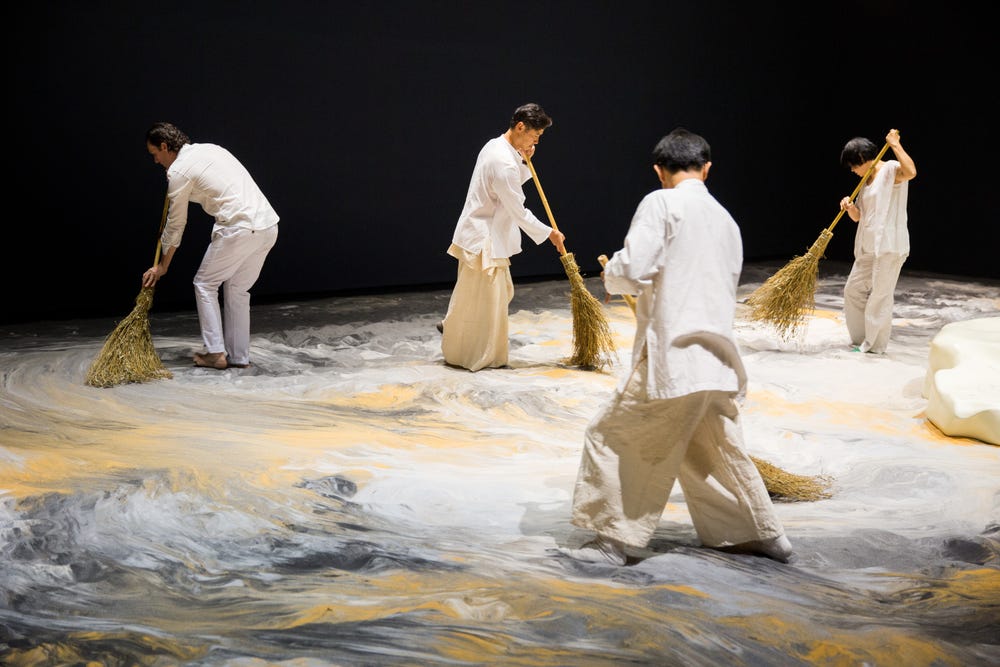 People with brooms moving sand during an art installation by Lee Mingwei