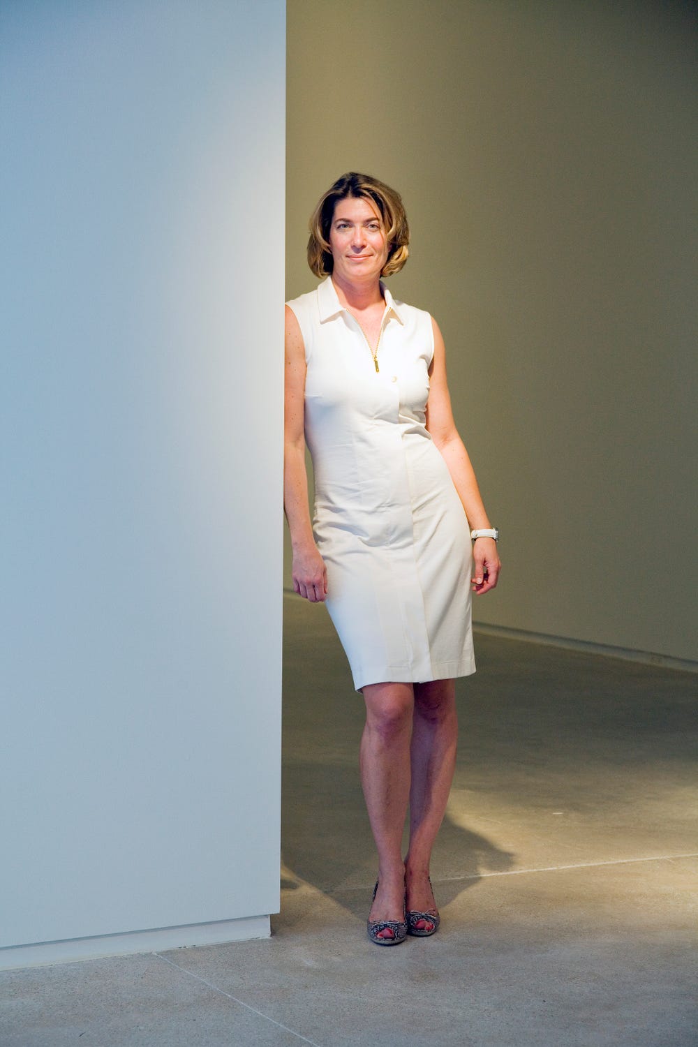 Photograph of woman in white dress leaning against wall.