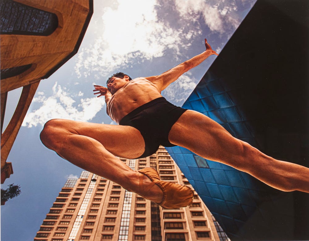 male dancer leaping, shown from below, with buildings in the background