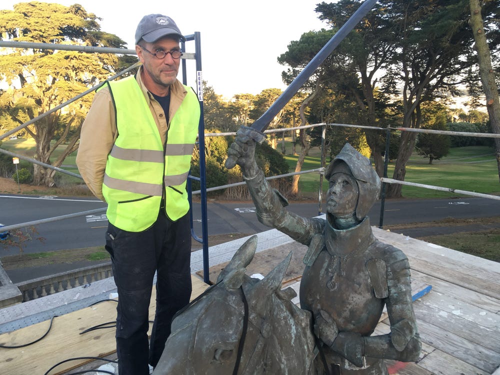 Man in a reflective vest standing next to a Joan of Art sculpture