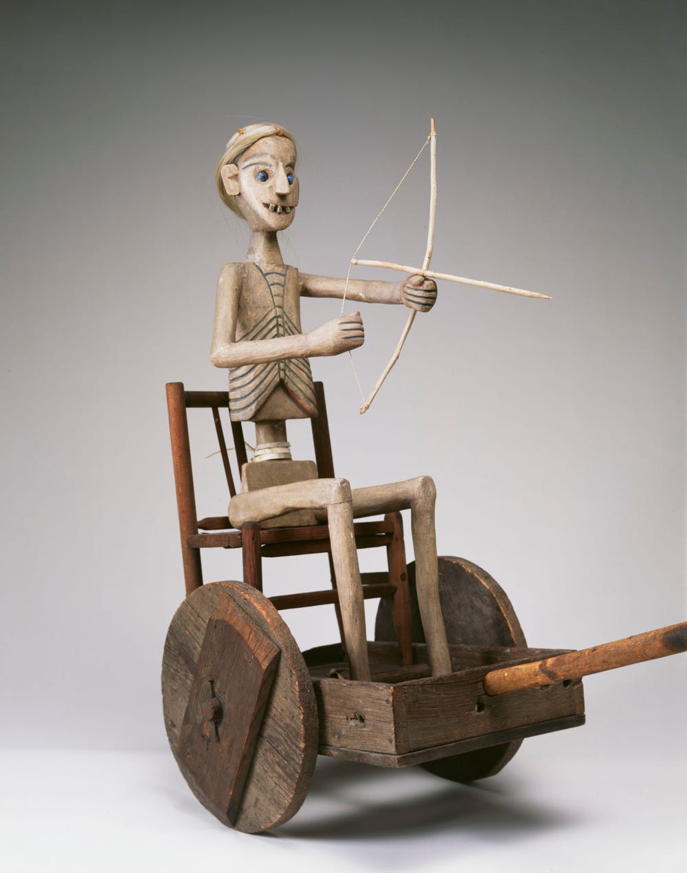 sculpture of a skeletal figure on a cart holding a bow and arrow