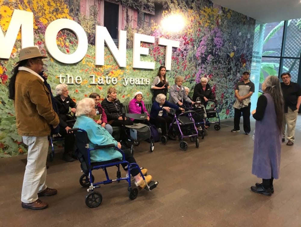 people listening to a woman present in front of Monet exhibit