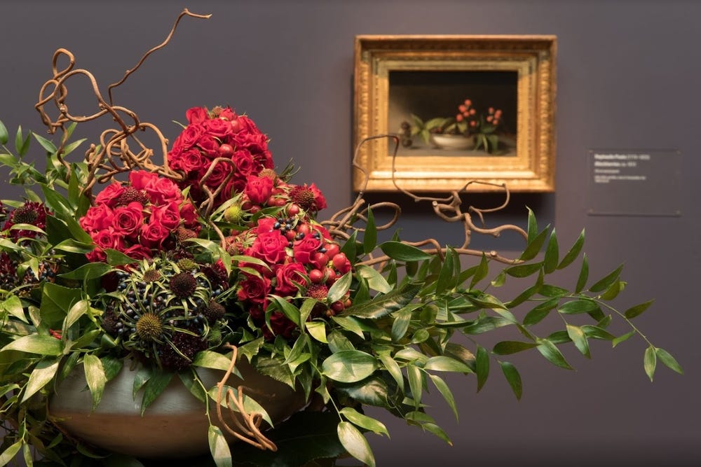 Photograph of red flowers in front of painting.