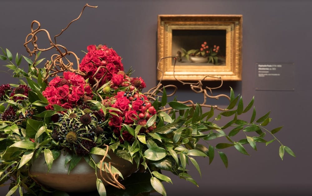 Photograph of red flowers in front of painting.