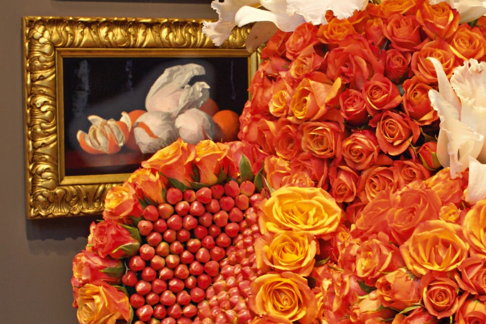 Photograph of red floral arrangement with corresponding painting in background.