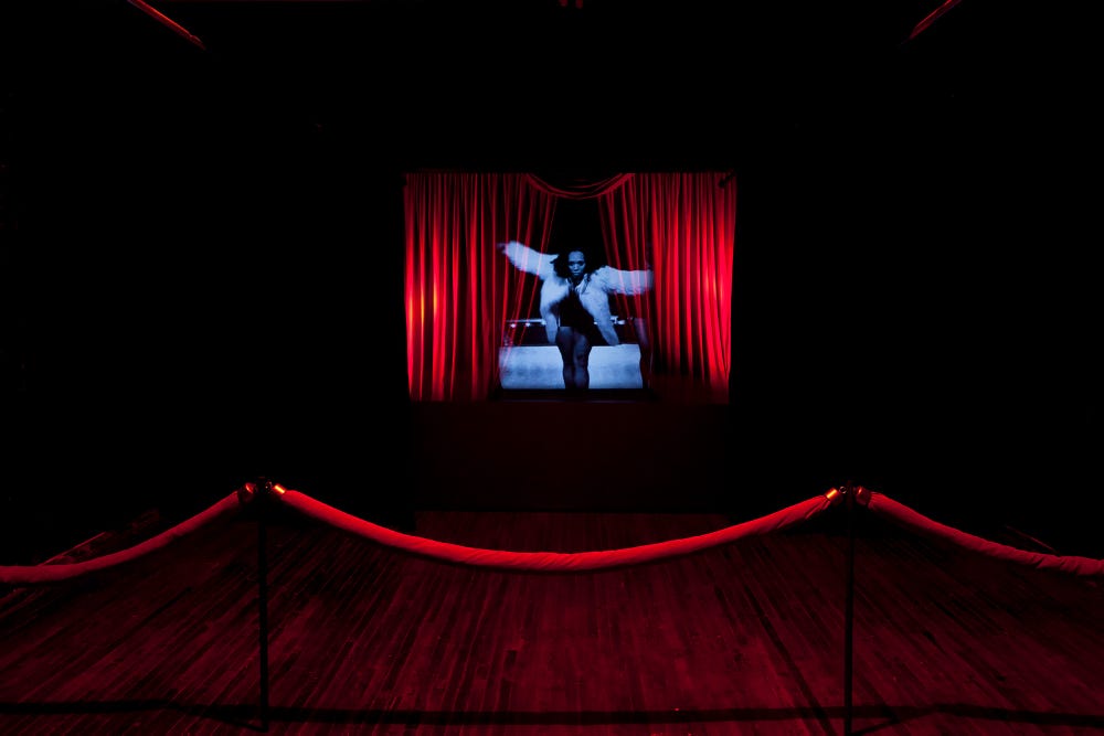 projection of a woman in black and white on a red curtain behind a red velvet rope