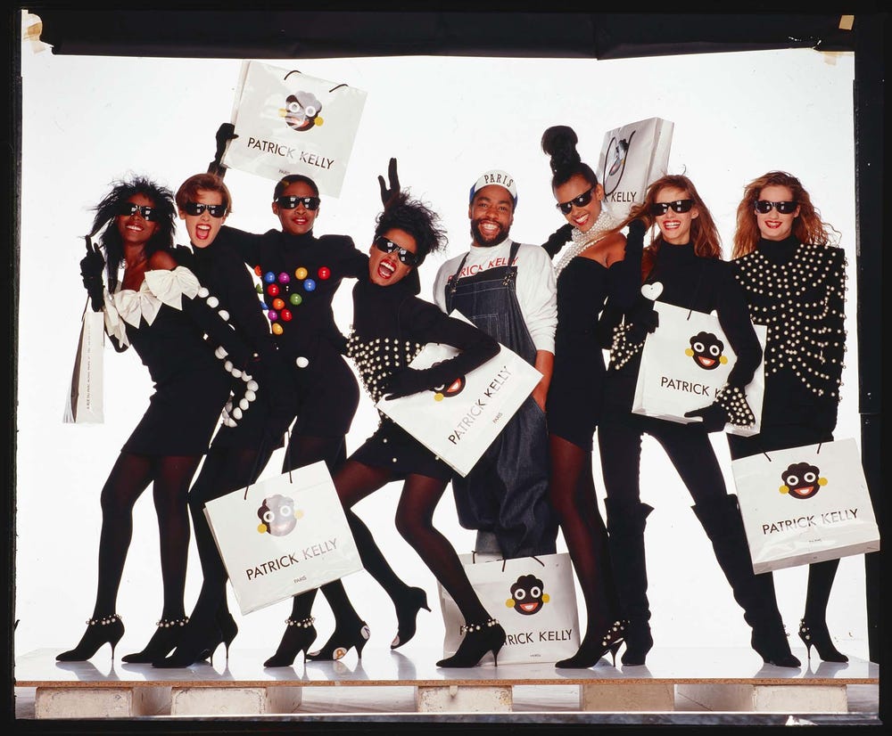 models and Kelly pose in black outfits with shopping bags featuring the golliwog