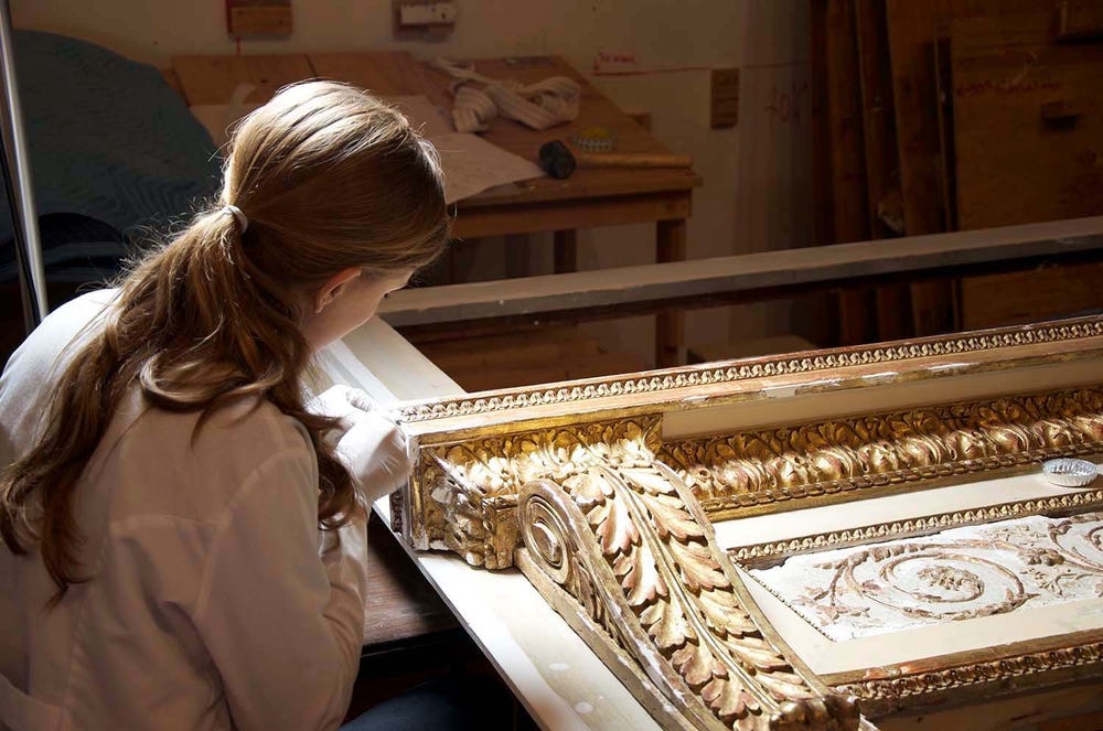 Photograph of person restoring intricate gold framed artwork.