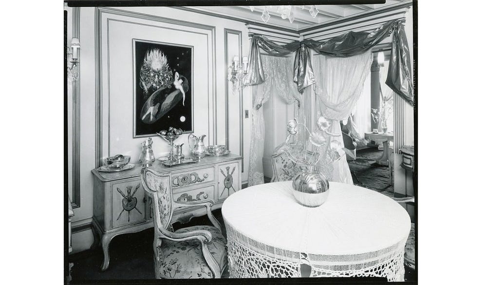 black and white image of a room with a table, vase, and chair, with artwork in the background