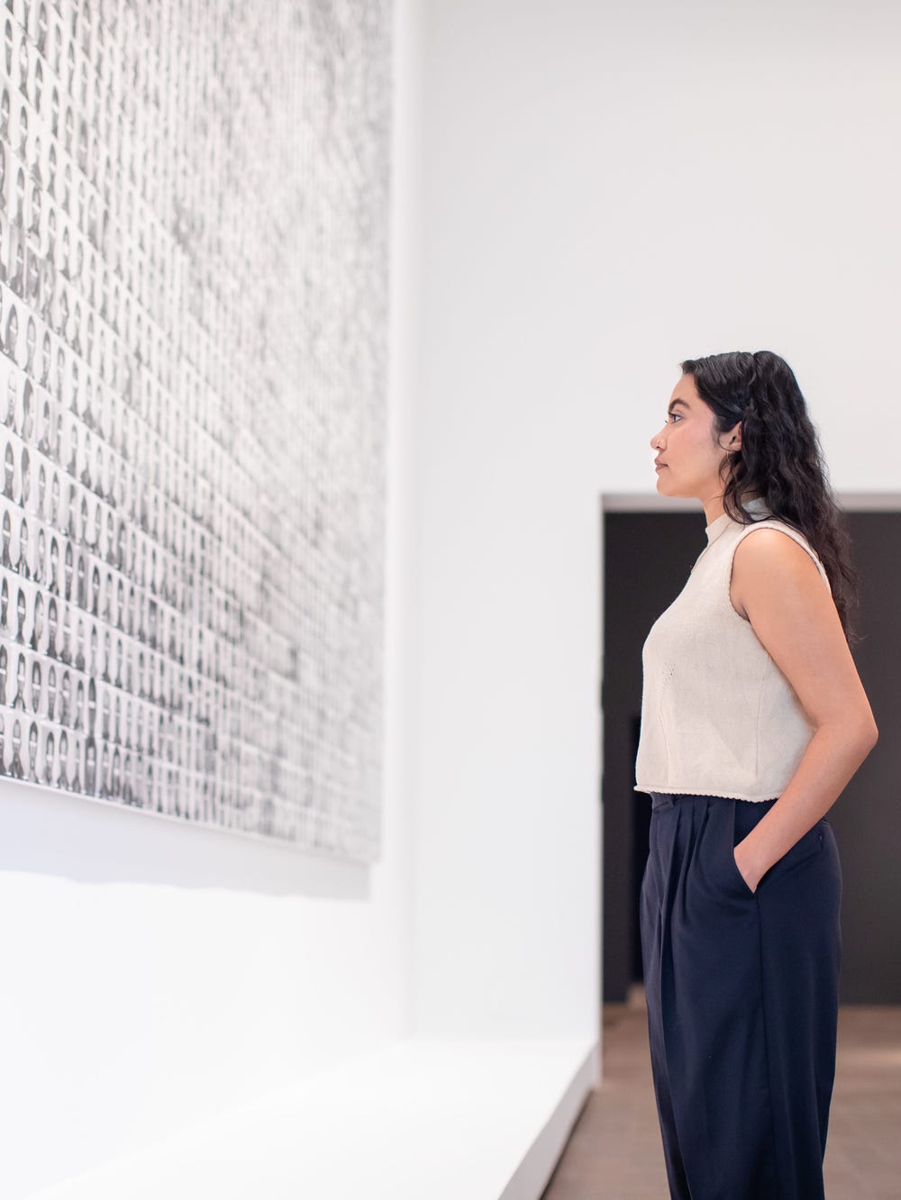 a woman looking at an artwork consisting of black and white headshots with eyes blocked out