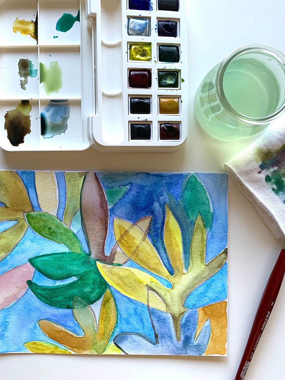 Paint and brush set next to colorful painting of leaves and flowers