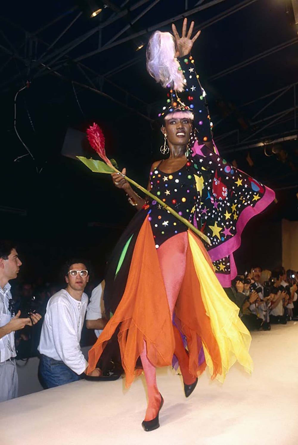 Model with her arm in the air on a runway wearing a bright costume