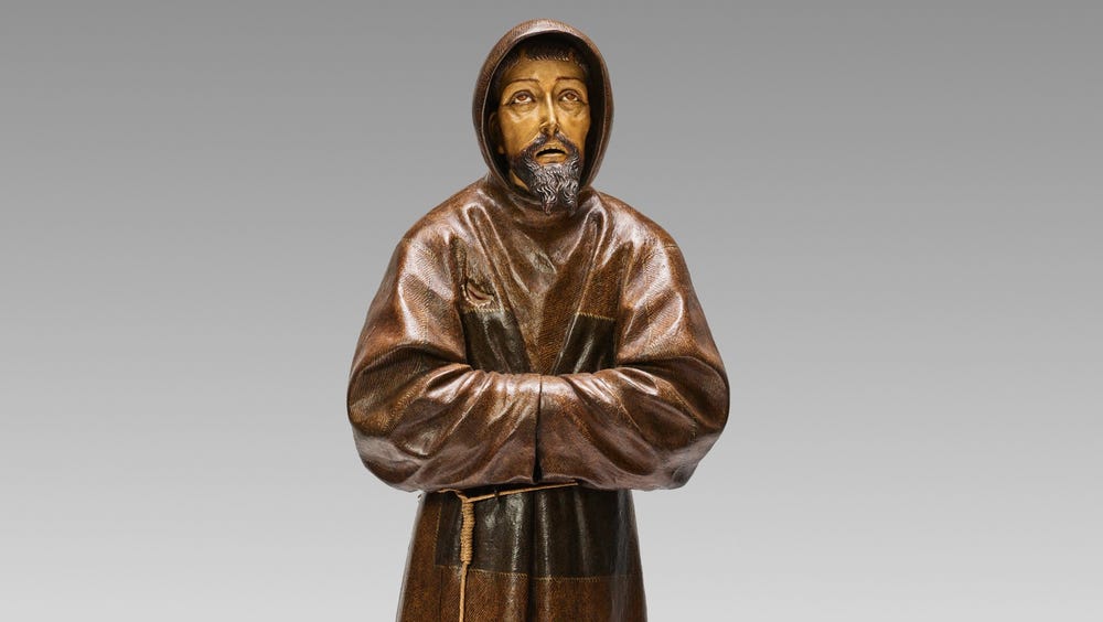 sculpture of a man in a robe with his sleeves together, looking up