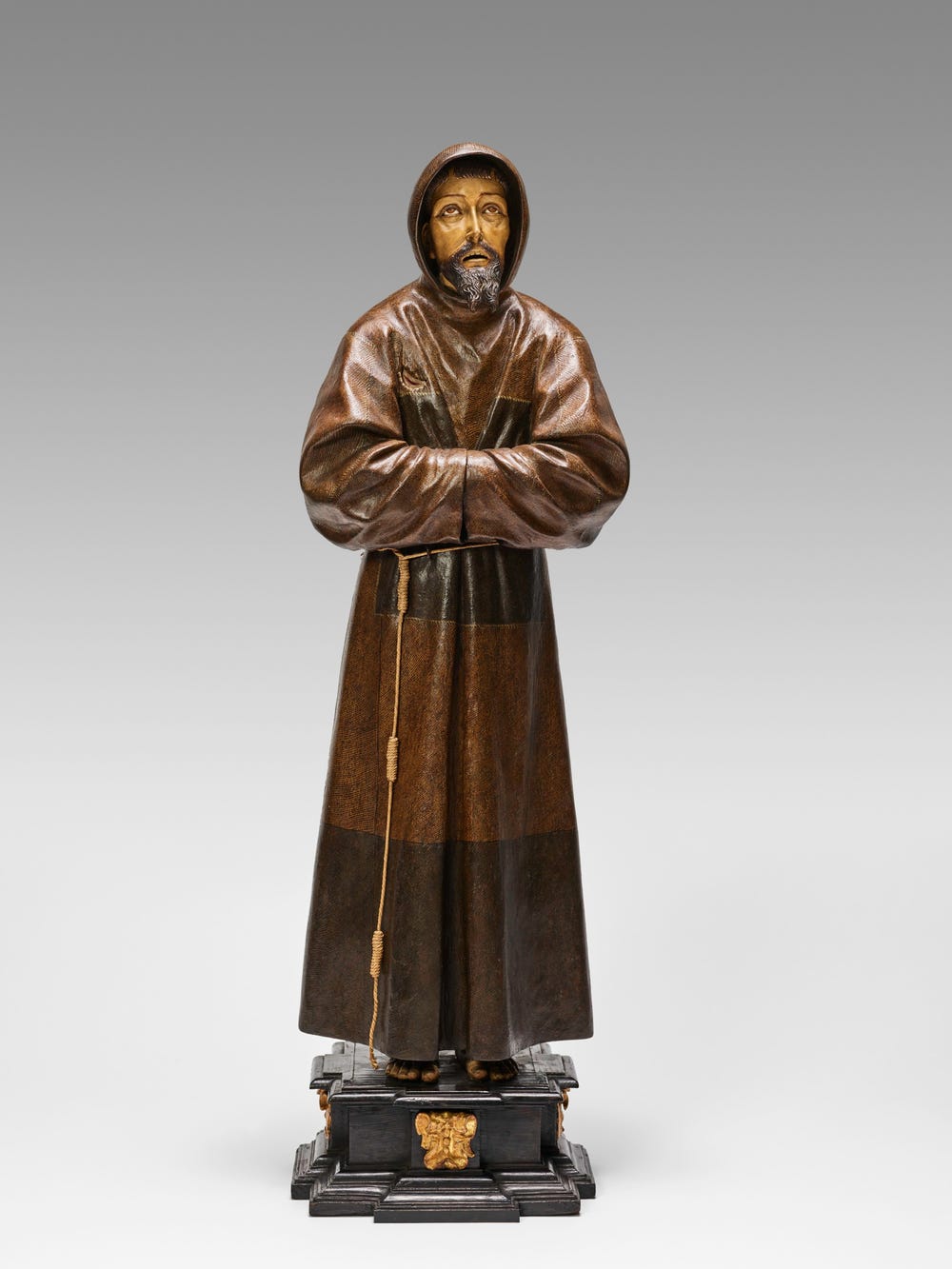 sculpture of a man in a robe with his sleeves together, looking up