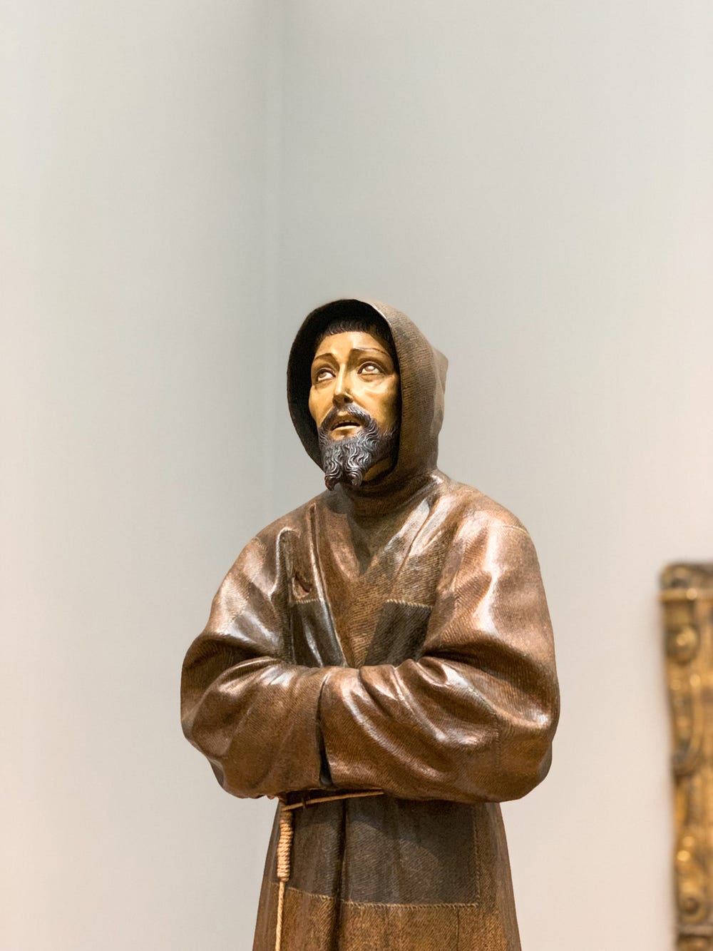 top half of sculpture of a man in a robe looking up with his sleeves together