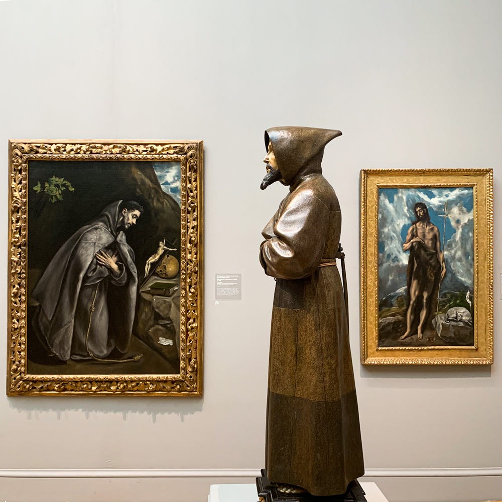side view of a sculpture of a man in a robe, with two paintings in the background