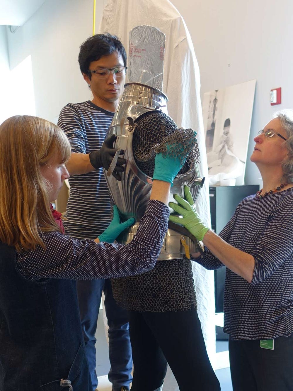 Objects conservators Colleen O’Shea and Jane Williams and mountmaker Mike Lai check the fit of the armor on its modified support and how well new mounts are supported.
