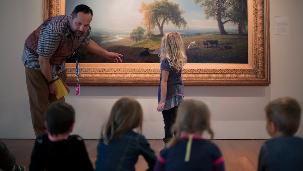 man showing landscape painting to a group of children