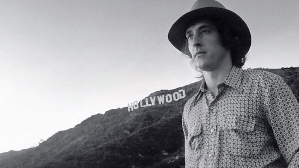 black and white image of Ed Ruscha in front of the Hollywood sign