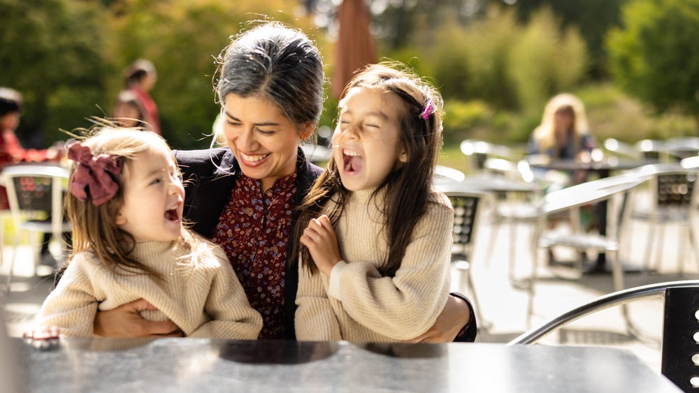 Mother and two daughters laughing at a table outside