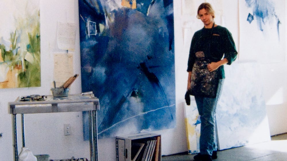 Woman standing in art studio next to blue painting