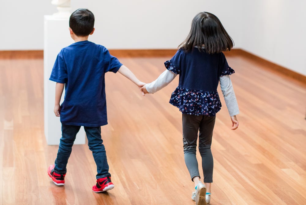 Two kids holding hands and walking through de Young museum