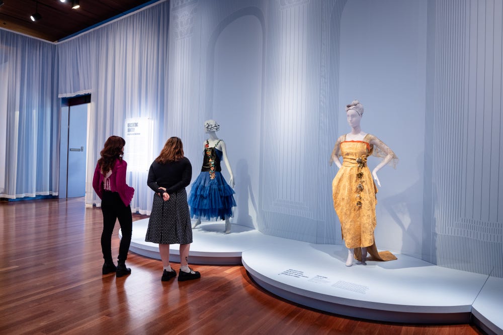 People looking at Fashioning San Francisco dresses in a de Young gallery