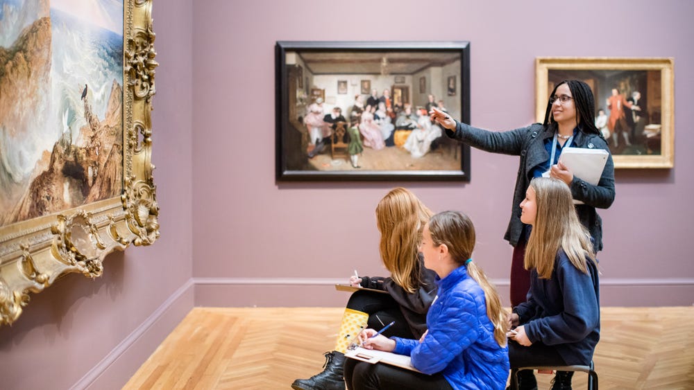 a teacher points to a painting and three students take notes