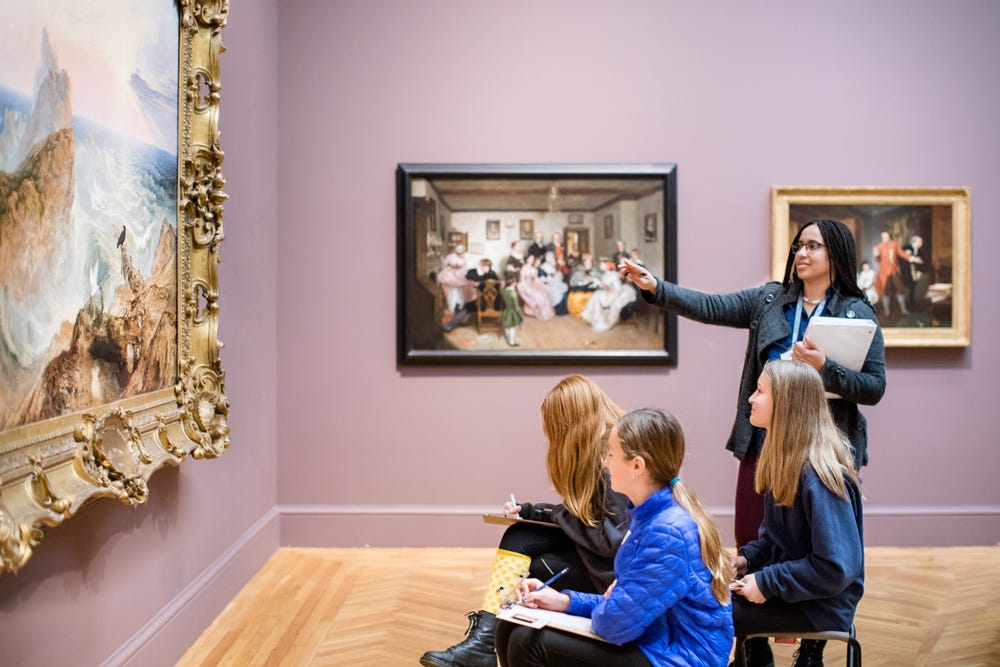a teacher points to a painting and three students take notes