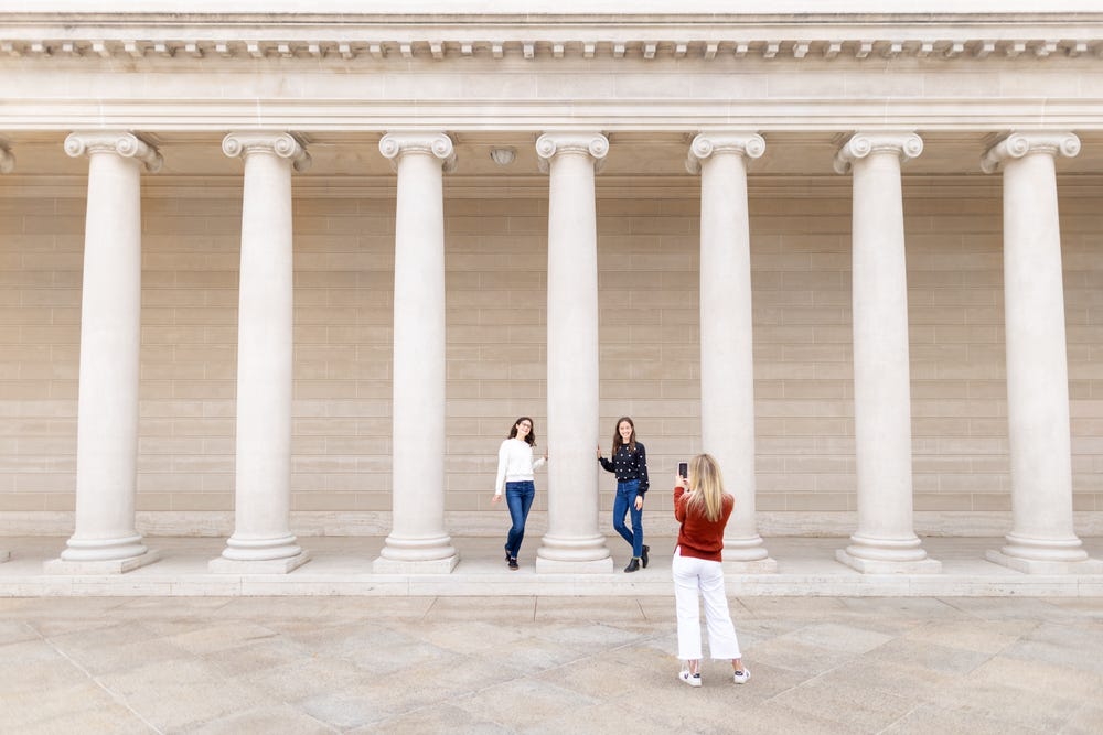 a young woman takes a photo of two other young women posing around a column