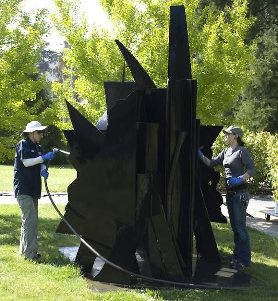 two people cleaning a black metal sculpture