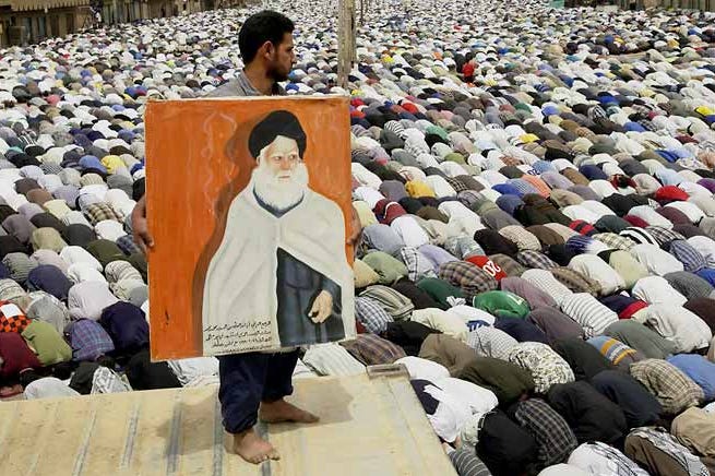 Man holding painting and watching a crowd pray.