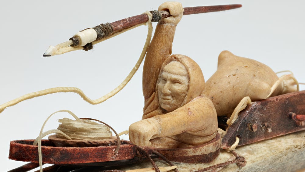 Sculpture of a person inside a kayak holding a spear