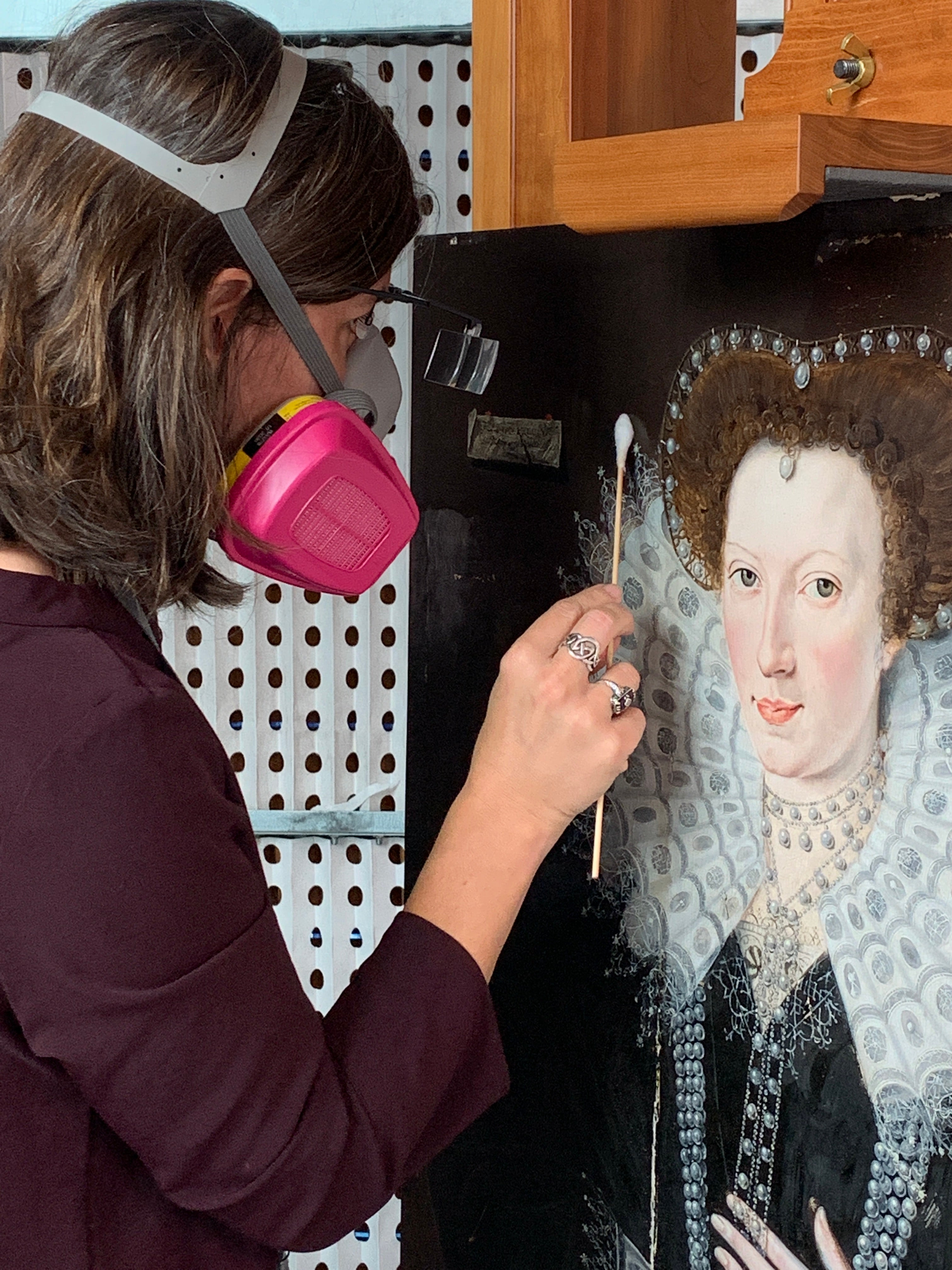 A woman wearing a face mask, working on conserving a painting