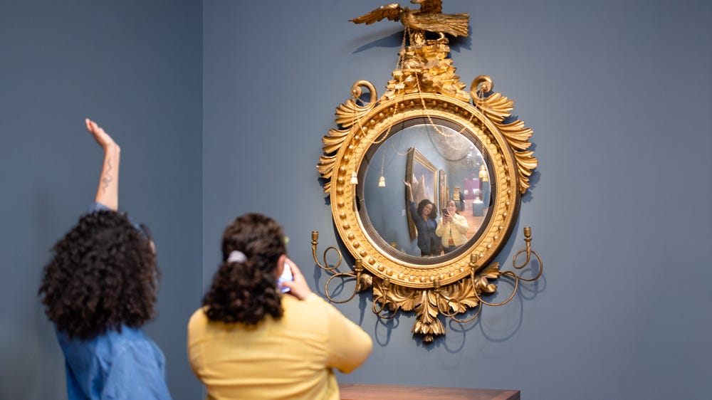 two young women take a selfie in a mirror in the gallery