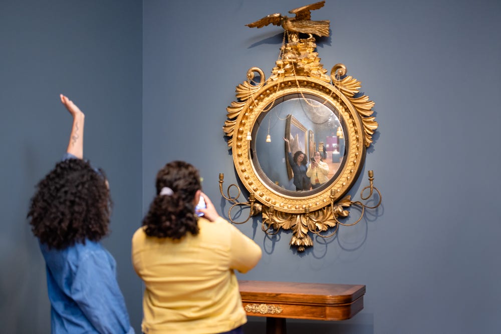 two young women take a selfie in a mirror in the gallery